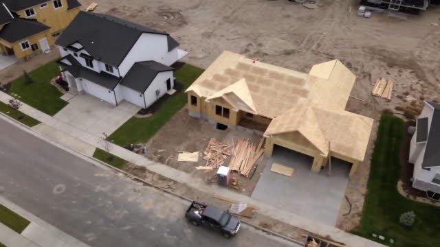 Arial shot of a newly constructed house with a black pick-up truck parked in front of in, next to a large completely finished two story white house next to another large, yellow two story home 