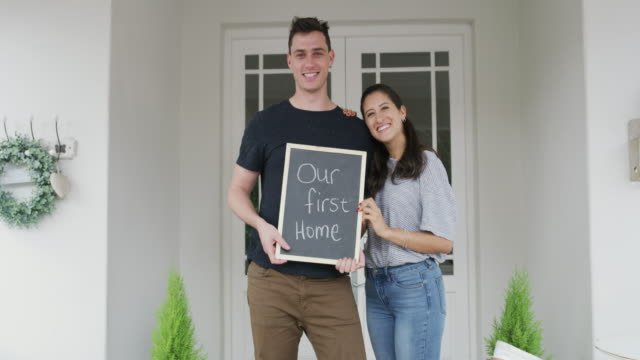 A couple holding up a sign (first home)