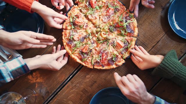 A group of people reaching for a slice of pizza