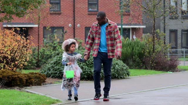 A black father walking his daughter around the neighborhood to trick--or-treat