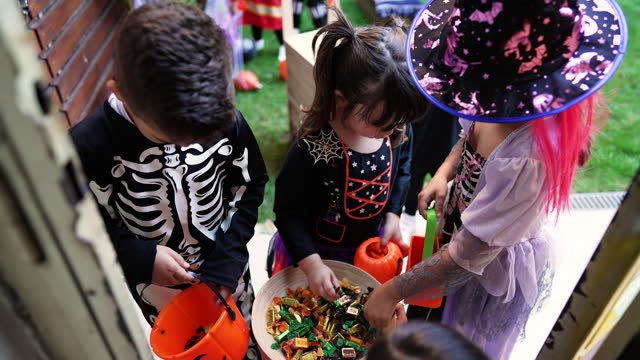 Three little kids in Halloween costumes digging in a bucket to grab Halloween candy. 