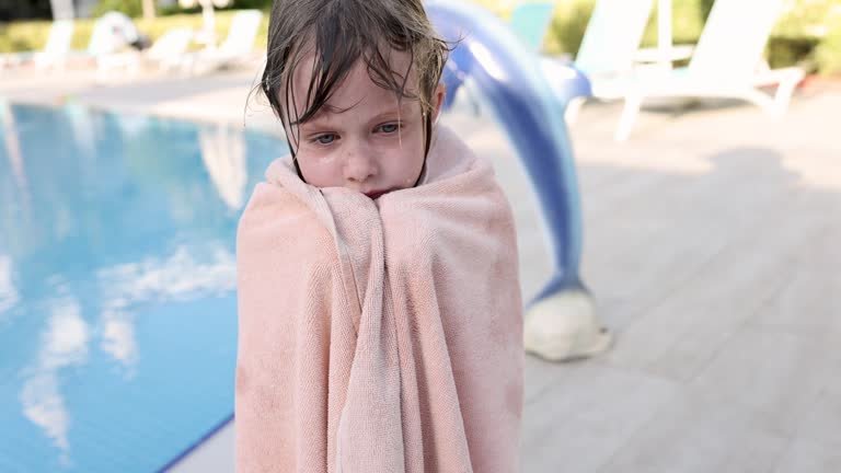 A little kid shivering in a pink towel 