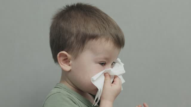 A little boy sneezing into a kleenex. 