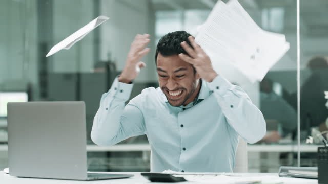 A male getting frustrated looking at a computer throwing paper in the air
