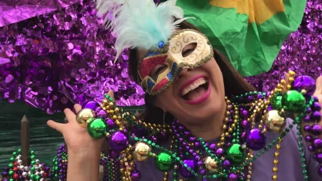 A white lady in a masquerade masks wearing a lot of beads with a huge smile on her face.