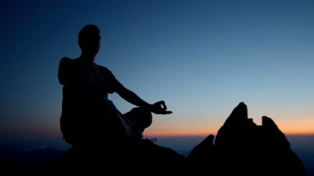 A person sitting on top of a mountain meditating.  
