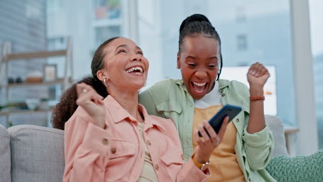 Two black girls looking at a phone, celebrating over good news. 