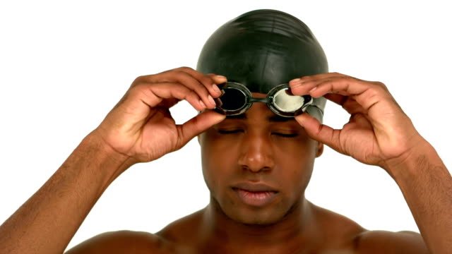 A man with a swimming cap on adjusting his goggles. 